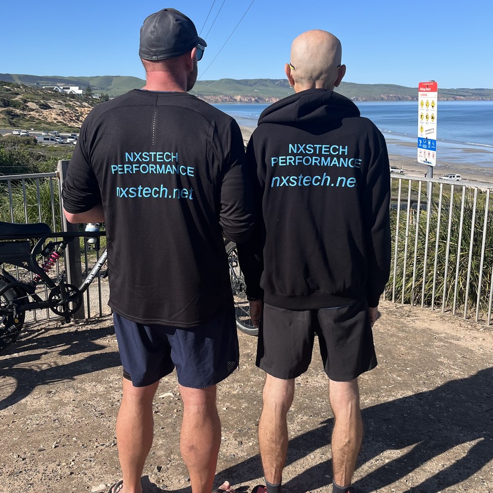 The backs of two shirts printed NXSTECH PERFORMANCE and nxstech.net, the beach behind them.